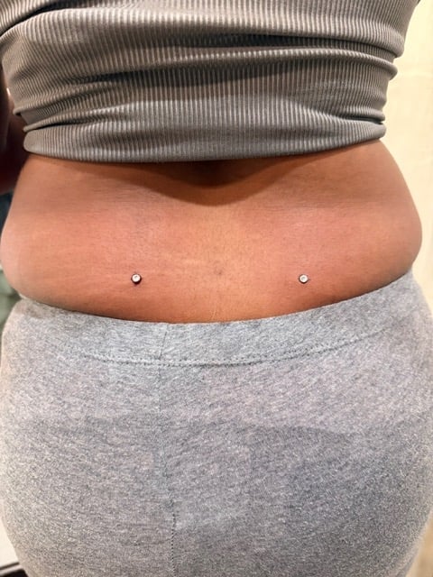 Person wearing gray clothing with two microdermal implants piercing the abdomen