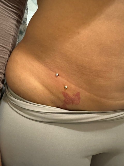 Close-up of torso showing belly button piercings and a small tattoo on the hip area