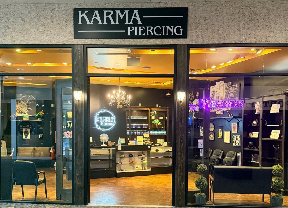 Storefront of Karma Piercing shop with illuminated windows displaying jewelry, piercings, and neon signage at night