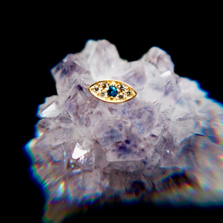 Gold evil eye pendant resting on raw amethyst crystal cluster against black background