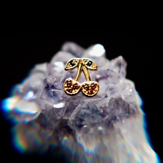 Gold cherry pendant on raw amethyst crystal cluster with iridescent lighting against black background