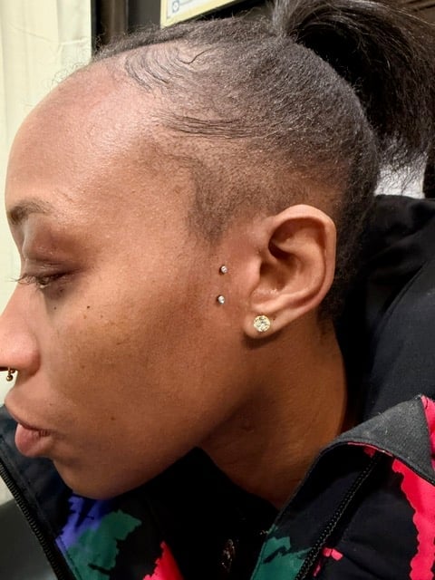 Side profile of a person with shaved head wearing colorful jacket with earrings and nose ring