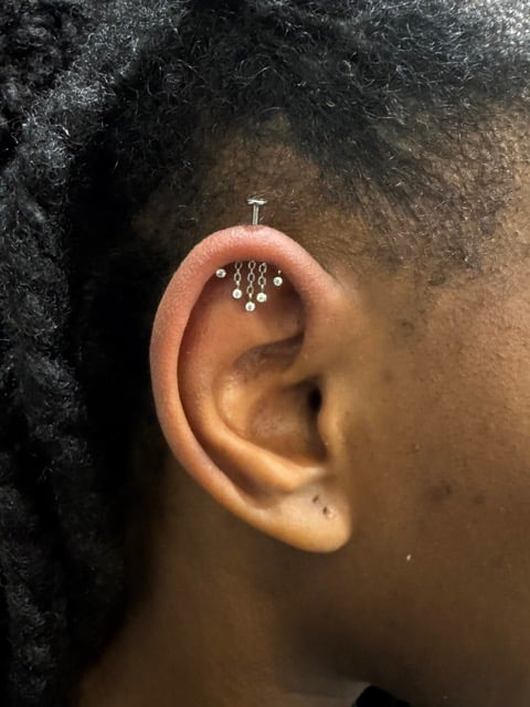Close-up of an ear with a decorative silver piercing on the upper cartilage featuring small dangling crystals
