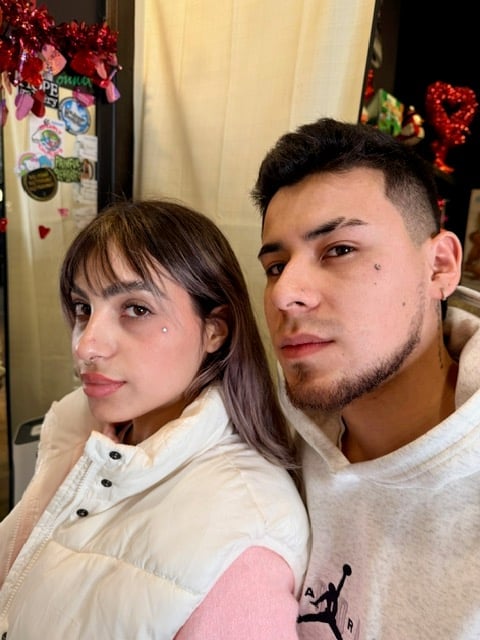 Two people posing together indoors with holiday decorations visible in the background