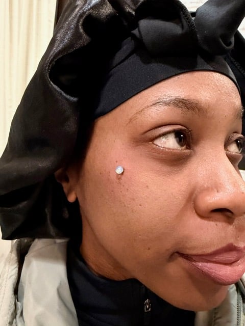 Close-up portrait of a person with a black bow in their hair, small facial mole, and neutral expression looking to the side