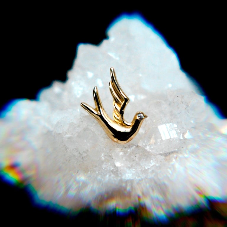 Gold bird-shaped pendant resting on white crystalline mineral cluster against black background