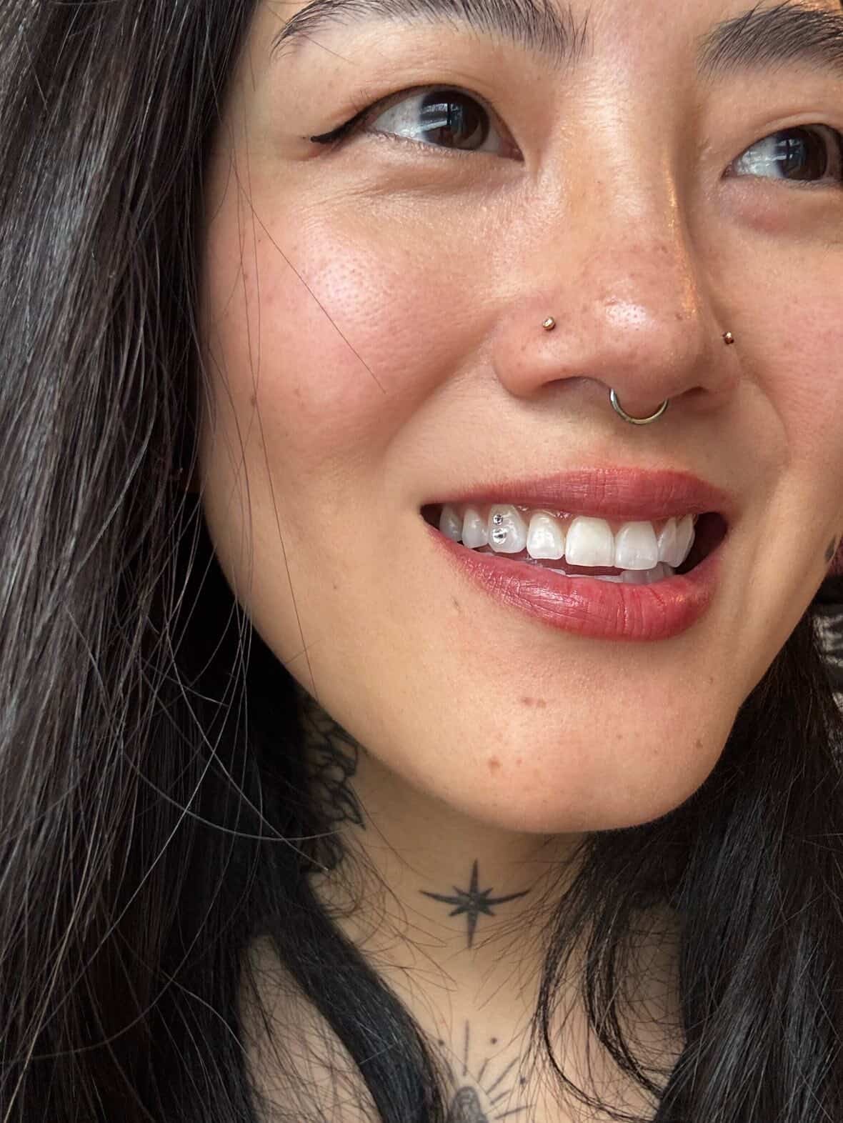 Close-up portrait of a smiling woman with long dark hair, nose ring, and chest tattoo